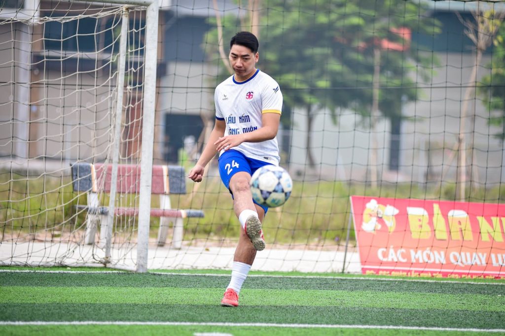 Young male soccer player practicing a powerful kick on an outdoor artificial turf football field.